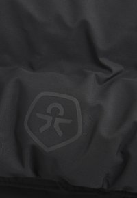Svart nylon tyg med en glänsande, präglad logotyp i sköldform, med en slät yta och minimala synliga sömmar.