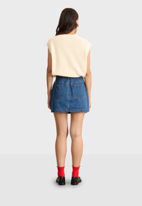 Jeansminikjol i ljusblått med framfickor och bakgodsömmar, matchad med en krämfärgad ribbad topp och röda knän-långa strumpor.