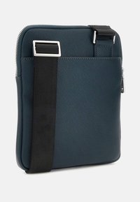 Borsa a spalla blu scuro realizzata in materiale testurizzato, con una cerniera argentata, una tracolla nera regolabile e un design elegante a forma quadrata.