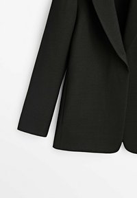 Blazer nero con una vestibilità su misura, rever affilati e un design delle spalle strutturato. Il tessuto ha una texture liscia e linee pulite.