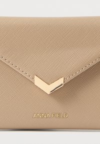 Beige synthetische clutch met een gestructureerde afwerking. Voorzien van een goudkleurige chevron-accent en een geperst merklogo aan de onderkant.