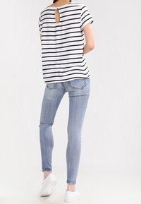 Top a righe bianco e blu navy a maniche corte con dettaglio a chiave sul retro, abbinato a jeans skinny azzurri chiari e sneakers bianche.