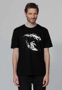 T-shirt noir avec un graphique blanc représentant un astronaute surfant sur une vague, sur fond d'étoiles. Manches courtes et coupe décontractée.
