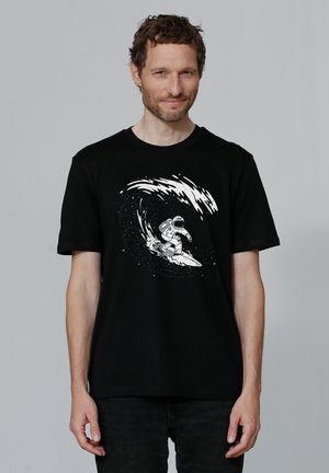 Zwarte T-shirt met een witte graphic van een astronaut die op een golf surft, tegen een achtergrond van sterren. Korte mouwen en een relaxte pasvorm.