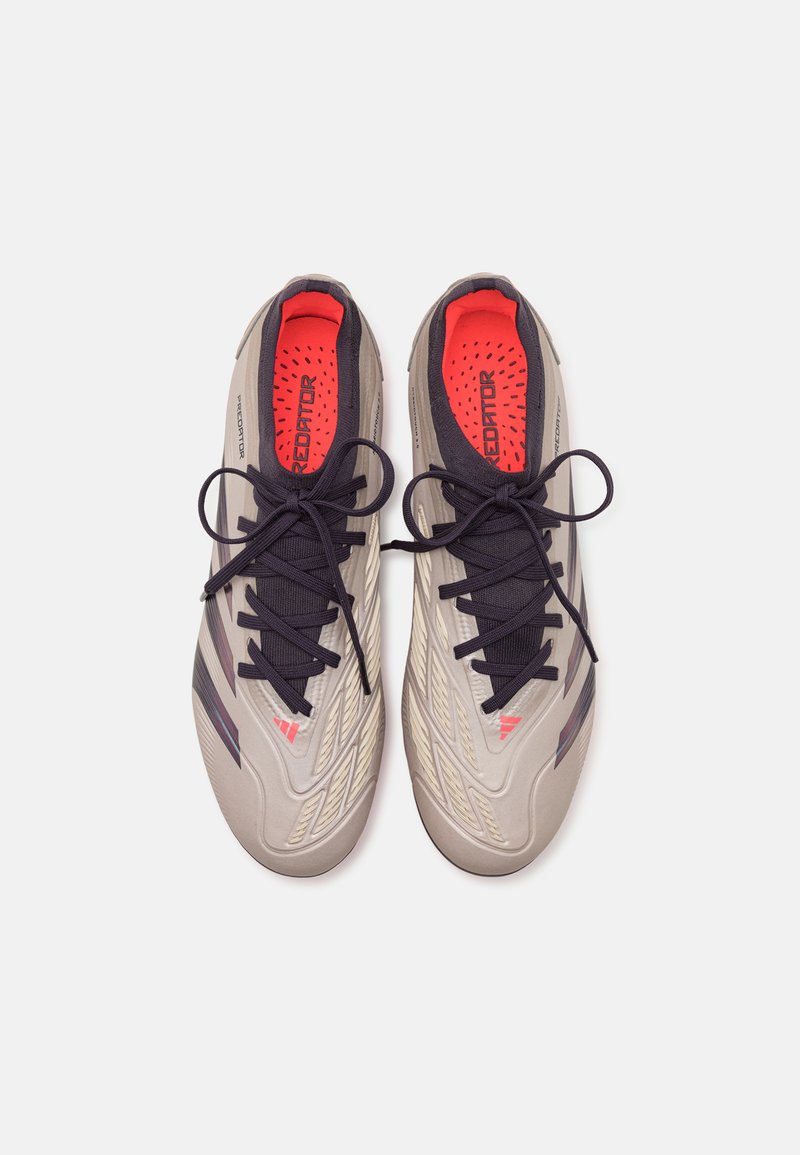 Des chaussures de football grises avec des lacets noirs et une doublure intérieure rouge, présentant des détails texturés et un design épuré. Matériau principalement synthétique.