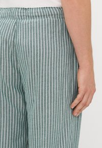 Heledad roheline ja valge triibuline püksid elastse vöökoha ja teksakanga peale; sale lõige, millel on õrn läige ja korralik õmblus.