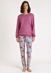 Lange mouw roze top gecombineerd met pyjamabroek met bloemenpatroon, waarop blauwe, roze en groene bloemen tegen een lichte achtergrond staan.
