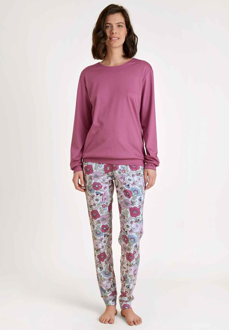 Lange mouw roze top gecombineerd met pyjamabroek met bloemenpatroon, waarop blauwe, roze en groene bloemen tegen een lichte achtergrond staan.