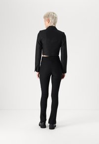 Blazer preto ajustado com mangas longas e costuras nas costas, emparelhado com calças pretas de cintura alta com um design justo e barra inferior arredondada.