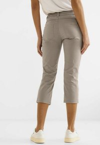 Ljusgrå, korta byxor med en slät textur, försedda med bakfickor och resårmidja. Matchade med vita sneakers, visade från baksidan.