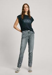 Crna majica s printom "PEPE JEANS" u srebrnoj boji, u kombinaciji sa svijetlosivim trapericama i srebrnim tenisicama. Pamuk, opušteni kroj.