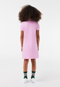 Vestido polo rosa con mangas cortas, corte recto y acabado texturizado, combinado con zapatillas blancas y calcetines verdes con rayas rosas.