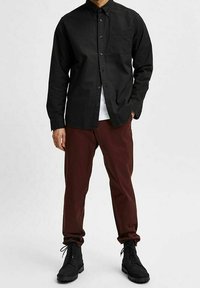 Zwarte lange mouwen knoopshirt met een borstzak, gecombineerd met bordeauxrode broeken en zwarte veterschoenen. Eenvoudig ontwerp en gestructureerde stof.
