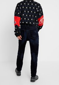 Pantaloni in corduroy blu scuro da uomo con una vestibilità slim, caratterizzati da un design della tasca posteriore e una finitura testurizzata, abbinati a una camicia in maglia con fantasia.