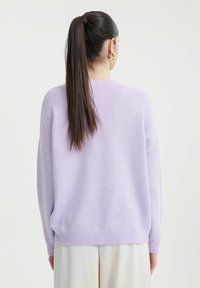 Fliederfarbener, oversized Pullover mit Strickstruktur, abgefallenen Schultern und geripptem Saum, kombiniert mit hellen Hosen. Einfaches, lässiges Design.