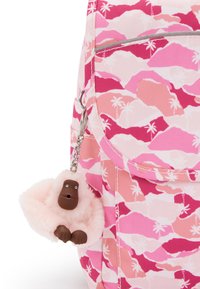 Sac à dos en tissu rose avec un motif de montagnes et de palmiers. Un porte-clés en gorille rose duveteux est attaché avec un anneau en argent.