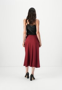 Débardeur en satin noir et jupe midi bordeaux à la texture lisse et fluide, associés à des chaussures à talons noirs.