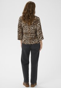 Leopardmönstrad topp med trekvartslånga ärmar, ihop med mörkgrå raka byxor och bruna skor. Texturerad tyg synlig.