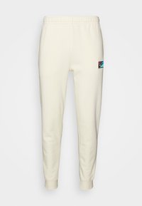 Cremefarvede sweatpants lavet af blødt stof, med elastisk talje, afsluttede ankler og et lille farverigt logo-patch.