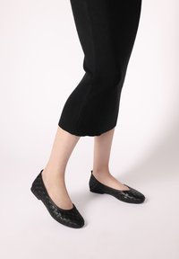 Schwarze, geflochtene Leder-Ballerinas mit abgerundetem Zehenbereich, niedrigem Absatz und flexibler Sohle, kombiniert mit einem schwarzen Rippstrickkleid.
