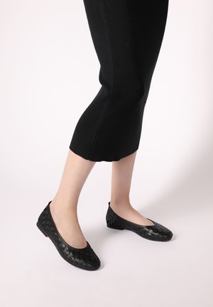Schwarze, geflochtene Leder-Ballerinas mit abgerundetem Zehenbereich, niedrigem Absatz und flexibler Sohle, kombiniert mit einem schwarzen Rippstrickkleid.