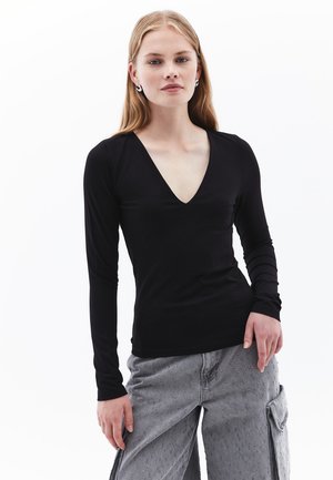 Zwarte lange mouw V-hals shirt gemaakt van een gladde, lichte stof, gecombineerd met grijze cargobroek met getextureerde accenten.