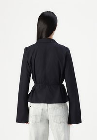 Black peplum jacket with a collar and long sleeves, featuring a fitted bodice and gathered waist, paired with light striped denim pants.