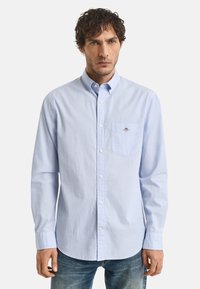 Himmelblaues, langärmliges Button-Up-Hemd aus Baumwolle mit Kragen, Brusttasche und kleinem Logodetail. Getragen mit blauen Jeans.
