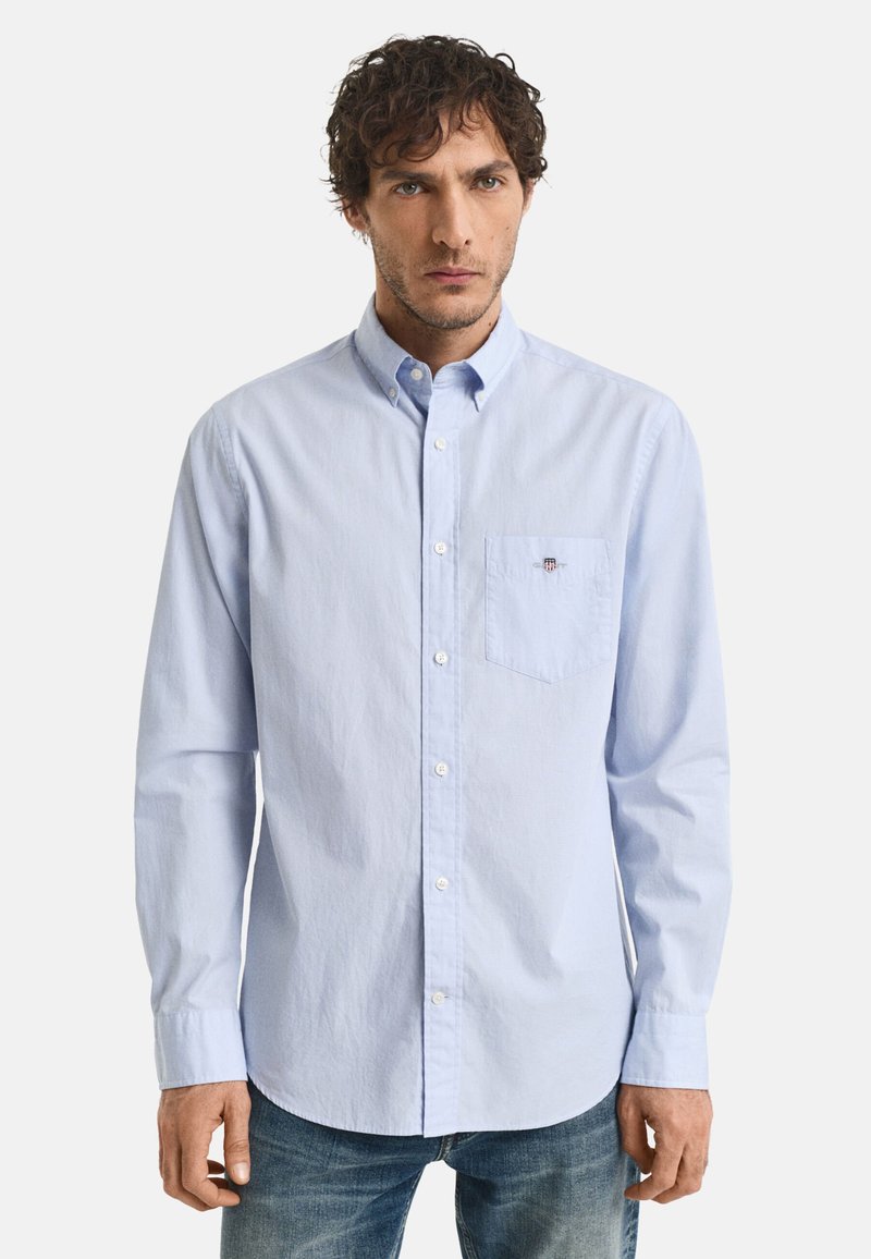 Himmelblaues, langärmliges Button-Up-Hemd aus Baumwolle mit Kragen, Brusttasche und kleinem Logodetail. Getragen mit blauen Jeans.