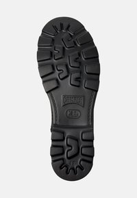Suela de zapato de goma negra con patrón texturizado para agarre, marcada con "CAMPER" y talla "42." Diseño duradero con bordes reforzados.