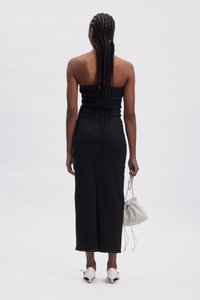Svart denim strapless kjole med en figursydd silhuett, kne-lengde, vertikale sømmer og en bakspalte, kombinert med hvite spisse hæler og en teksturert veske.