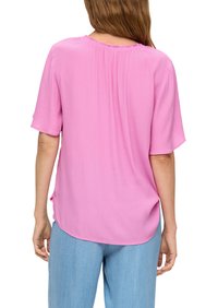 Lichte roze blouse met korte mouwen, ronde halslijn en zacht vloeiende stof. Draag met lichtblauwe denim broek. Soepele textuur, losse pasvorm.