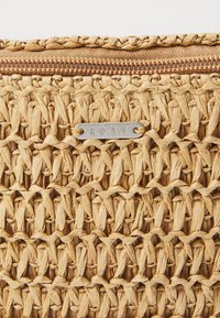 Woven straw purse with a textured, natural finish. Features a bronze zipper and a metallic brand tag labeled "ROXY."