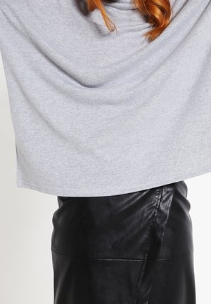 Haut drapé gris en tissu doux, associé à une jupe crayon en cuir noir taille haute, avec un détail d'ouverture sur le côté.