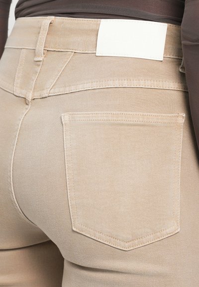 Beezžinsid, millel on pealeistutud siluett, valmistatud denimpinnast. Omadusteks on tagakotid ja lihtne valge nahkmark vööl.