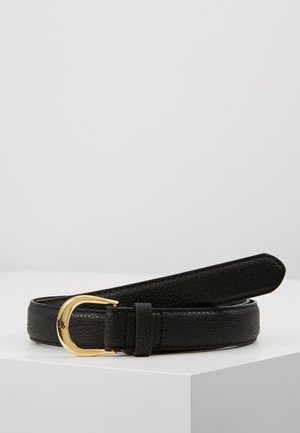 Ceinture en cuir noir texturé roulée avec une boucle dorée arrondie reposant sur une surface blanche contre un fond gris.