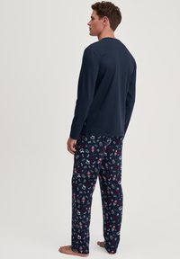 Marineblauwe lange mouw top met een ronde hals, gecombineerd met gestreepte pyjamabroek met feestelijke ontwerpen op een donkere achtergrond.