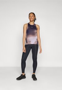 Ärmelloses Workout-Oberteil in Farbverläufen von Lila, kombiniert mit schwarzen Leggings. Verfügt über einen runden Halsausschnitt und eine figurnahe Silhouette.