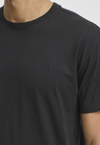 Fekete, crew-neck stílusú póló puha pamutból. Diszkrét hímzett logóval a bal mellkason. Rövid ujjak és laza fazon jellemzi.