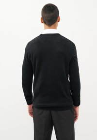 Čierny pletený sveter s okrúhlym výstrihom, dlhými rukávmi a rebrovanými manžetami; nosený cez bielu košeľu s golierom; hladká textúra.