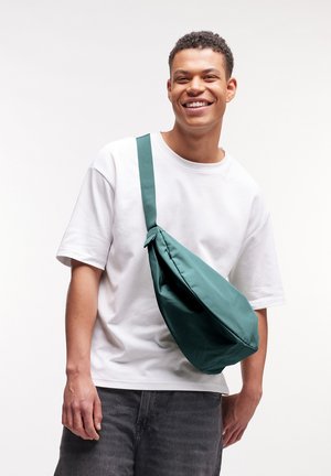 Borsa a tracolla verde realizzata in tessuto resistente, con una lunga tracolla, texture liscia e forma arrotondata. Indossata a tracolla.