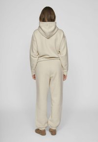 Sudadera beige con cordón y corte relajado, combinada con pantalones cónicos a juego. Tejido suave y texturizado; puños elásticos en los tobillos.