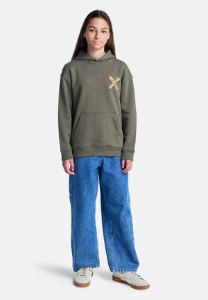 Sweat à capuche vert olive avec une poche kangourou à l'avant, graphique jaune sur la poitrine, associé à un jean en denim bleu à jambes larges et à des baskets beiges.