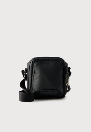 Sac bandoulière rectangulaire noir avec une large sangle réglable, une poche avant zippée et des compartiments latéraux, sur un fond clair uni.
