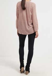 Blusa a maniche lunghe con motivo nei colori rosso, rosa e bianco, abbinata a jeans skinny scuri. La blusa presenta una vestibilità ampia e polsini elasticizzati.