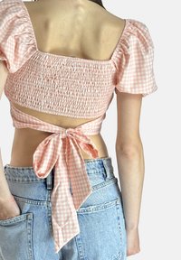 Top corto a quadretti rosa chiaro con maniche a sbuffo, schiena smock e un fiocco annodato in vita, abbinato a pantaloni corti di jeans a vita alta.