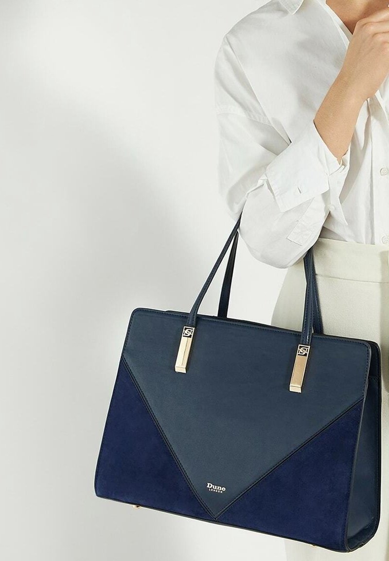 Granatowa skórzana torebka z zamszu z geometrycznym wzorem, złotymi akcentami, podwójnymi uchwytami oraz logiem na przodzie.