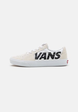 Beżowe zamszowe sneakersy z białymi tekstylnymi akcentami. Duże czarne logo "VANS" po boku. Biała gumowa podeszwa, zaokrąglony nosek i sznurowany design.