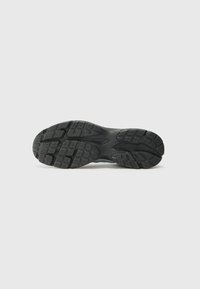 Zwarte sneakerzool met getextureerde grippatronen, voorzien van gegoten rubber en contouren voor ondersteuning. Minimalistisch ontwerp met duidelijke loopvlakdetails.