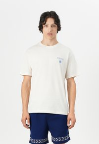 Crème-kleurig katoenen t-shirt met een ronde hals, korte mouwen en een blauwe bedrukking van het ontwerp "MYKONOS" aan de linkerkant.